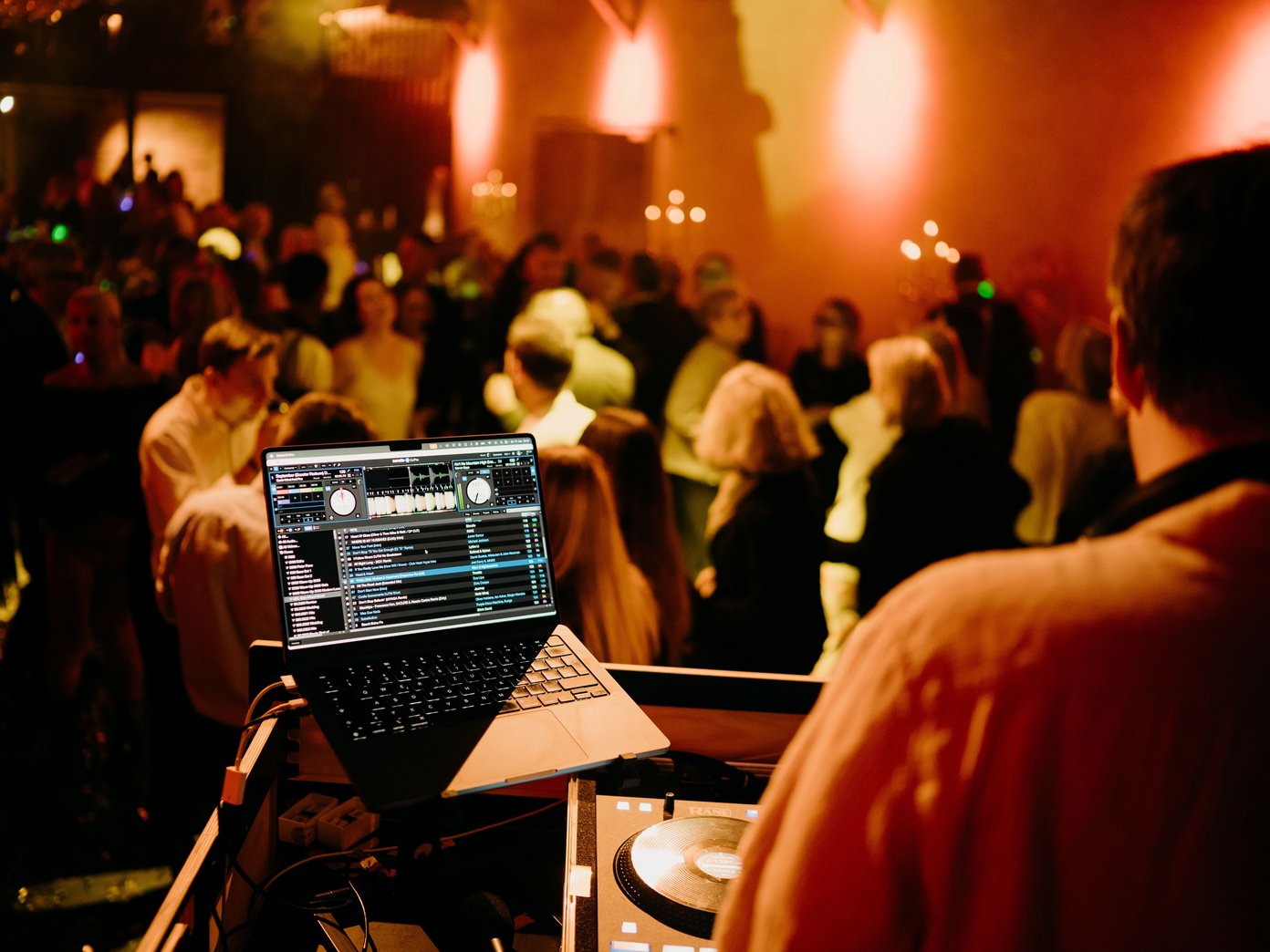 DJ Pult auf einer Bühne vor tanzenden Menschen